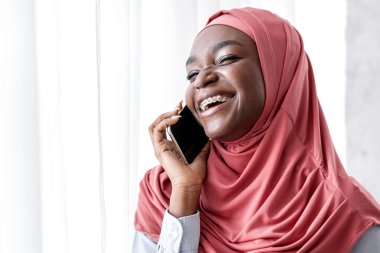 Rahatlamış Sabah. Keyifli siyahi kadın tesettürlü kahve içiyor, cep telefonuyla konuşuyor, pencerenin yanında arkadaşlarıyla konuşuyor, hoş sohbetler yapıyor, diş telleri takıyor, uzay kopyaları yapıyor.