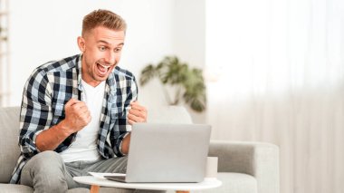 Çevrimiçi galibiyeti kutlayan aşırı neşeli yakışıklı adam, dizüstü bilgisayara bakarak büyük başarı ya da iş başarısı, boş alan