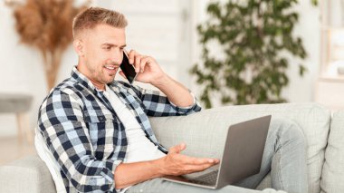 Rahat bir iş yeri. Akıllı telefonda konuşan, dizüstü bilgisayarda çalışan, kanepede uzanan sıradan bir genç.