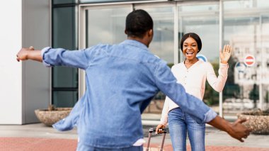 Mutlu Afrikalı kız havaalanına indikten sonra erkek arkadaşıyla buluşuyor, el sallıyor, sarılmaya hazır, seçici bir şekilde odaklanıyor.