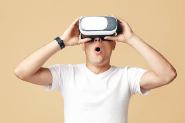 Modern teknoloji, eğlence ve sanal dünya. Şaşırmış zoomer erkek öğrenci beyaz tişörtlü, akıllı saat ve vr gözlüklü açık arka planda izole edilmiş boş bir alana bakıyor.