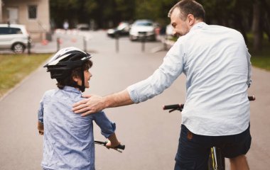 Baba ve oğlunun arka plan bulanık bir şekilde parkta bisiklet sürerken çekilmiş dikiz görüntüsü.
