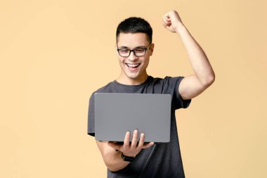 Harika iş çıkardın, sorunu çözdün ve oyunu kazandın. Gözlüklü mutlu genç öğrenci dizüstü bilgisayara bakar ve zafer duygularını bej arka planda izole edilmiş bir şekilde ifade eder.