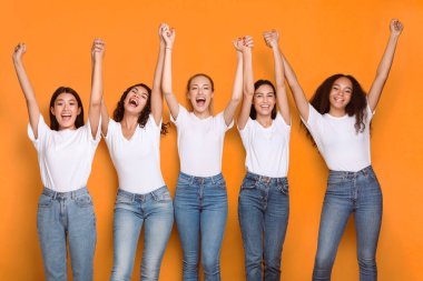 El ele tutuşan çeşitli kızlar, sarı arka planda duran kameraya gülümsüyor. Stüdyo Çekimi