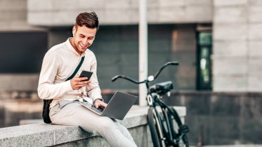 Yürüyüş, iş ve smm, arama bilgileri ve dışarıdaki sosyal ağlar. Gülümseyen genç ve çekici bir hippi. Serbest çalışan. Kablosuz kulaklıklarla sokakta oturuyor.