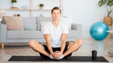 Karantina süresince evde tek başına modern sporlar. Gözleri kapalı adam oturma odasının içinde yoga yapıyor ya da yapıyor.