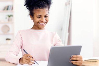 Çevrimiçi Öğrenme. Neşeli siyahi ortaokul öğrencisi kız evde dijital tablet kullanıyor. Seçici Odaklanma