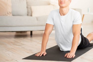 Yoga ve esneme egzersizleri. Spor kıyafetli barışçıl bir adam oturma odasında egzersiz yapıyor, boş yer var.