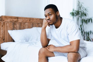 Evdeki yatak odasında yatakta oturan mutsuz siyah adam. Hayat Sorunlarını Düşünen Depresyonlu Afrikalı Amerikalı. Stres, ilgisizlik ve erkek depresyonu kavramı. Metin için Boş Alan