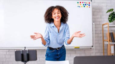 Evde eğitim ve uzaktan öğrenim. Gülümseyen Afrikalı Amerikalı kız jest yapıyor ve evdeki web kameralarına bakıyor. Öğrencilerle konuşuyor.