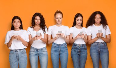 Çeşitli Kızlar Sosyal Medya Uygulamalarında Smartphone Kullanıyor Sarı Arkaplanda Duruyorlar. Modern İletişim. Stüdyo Çekimi