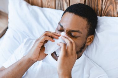 Hasta Afrikalı Amerikalı adam, kağıt mendille burun sümkürerek evde yatıyordu. Kara Adam 'ın Rhinitis, Grip ve Grip Hastalığı Belirtileri. Soğuk Kafada Kavram.
