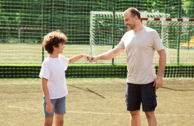 Harika iş çıkardın. Yakışıklı, olgun bir adamın çocuk futbol sahasına yumruk tokuşturuşunun yan görüntüsü.