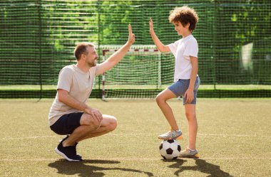 Çak bakalım. Yakışıklı yetişkin bir adamın çocuğuyla sahada futbol oynadığı yan manzara.