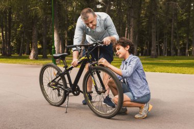 Doğada makasla bisiklet tamir eden gülümseyen adam ve çocuğun tam boy portresi.