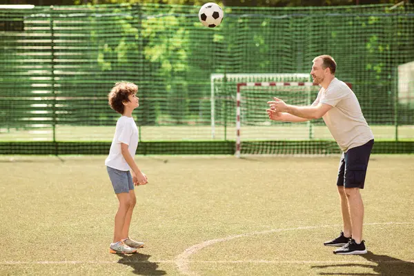 Aktif Yaşam Tarzı Konsepti. Sportif bekar bir babanın oğluyla futbol oynarken, futbol sahasında topu oğlana atarken, aile birlikte vakit geçirirken yan görüntüsü. Rekreasyon