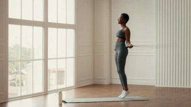 Genç bir Afrikalı Amerikalı kadın atlama halatı egzersizi yapıyor, atletizmini gösterirken sağlıklı bir yaşam tarzını geliştiriyor. Parlak oda, rutininin enerjik atmosferini arttırıyor..