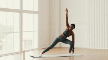 Bir atletik milenyum kadını evinde spor salonunda egzersiz yapıyor. Doğal ışığın içeri girmesinin keyfini çıkarırken spor rutinini sürdürmeye odaklanmış..