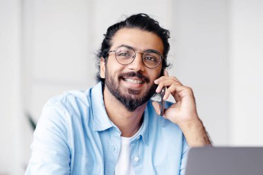 Neşeli Hintli, serbest çalışan, kahve içen, cep telefonuyla konuşan, iş yerinde laptopla çalışan, arkadaşlarıyla konuşan, iş yerinde dinlenen, boş alan olan bir adam.