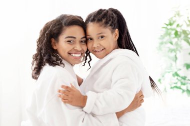 Mutlu siyah aile portresi, bornozlu mutlu anne ve kızı, neşeli genç Afrikalı anne ve çocuğu birlikte vakit geçiriyorlar, kucaklaşıyorlar ve kameraya gülümsüyorlar, uzay kopyaları yapıyorlar.