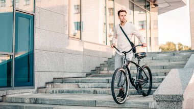 Genç bir adam şehir ortamında bisikletiyle merdivenlerden iniyor. Gelişigüzel giyinerek, rahat bir yaşam tarzını kucaklarken açık havanın tadını çıkartıyor..