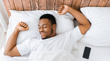 Günaydın konsept. Evdeki yatak odasında uyuduktan sonra yatağında uzanan ve ellerini esneten siyah adam. Adam yatakta uyanıyor, dinleniyor ve dinleniyor. Panorama, Yüksek Açılı Görünüm