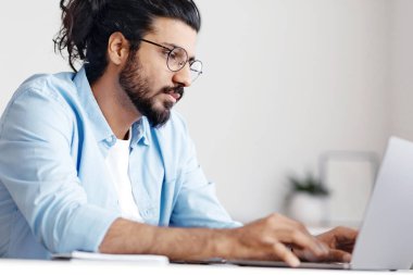 Ofiste dizüstü bilgisayarda çalışan genç Doğu çalışanı, işyerinde oturan, klavyede yazan, bilgisayar ekranına bakan, çevrimiçi projeyi kontrol eden, boş alanı kontrol eden meşgul Arap erkek girişimci.