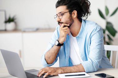 İçişleri Bakanlığı 'nda dizüstü bilgisayarla çalışan düşünceli Hintli serbest çalışan, bilgisayar ekranına bakan, proje çözümünü düşünen, internette bilgi tarayan,