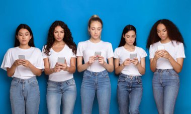 Sosyal medyada telefonda sohbet eden beş farklı milenyum kadını Blue Studio 'nun arka planında dikiliyor. Akıllı Telefonlu Ciddi Kadın Mesajlaşma veya Cep Telefonu Uygulamaları Kullanımı