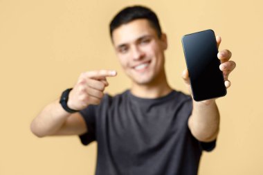 Blog yazarından harika bir eleştiri, reklam ve tavsiye. Kahverengi tişörtlü mutlu erkek öğrenci uygulamayı ve telefonu boş ekranla göstermeyi öneriyor, bej arka planda izole edilmiş, stüdyo çekimi