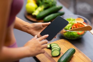 Kilo Verme Uygulaması. Tanımlanamayan bir kadın cep telefonunu boş ekranlı kullanıyor, yemek pişiriyor ve evdeki modern mutfakta sağlıklı yemek hazırlamak için yemek tarifi arıyor. Kırpılmış, Mockup