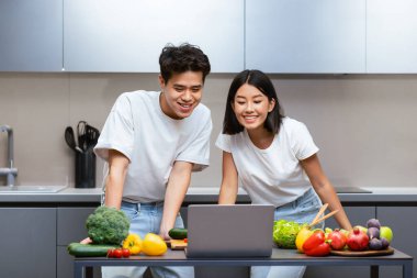 Mutlu Çinli çift laptoplarını birlikte yemek pişiriyor yemek tariflerini evde, modern mutfaklarda tarıyor. Yemek pişirme sitesi ve blog, Yemek Hazırlama Konsepti. Seçici Odaklanma