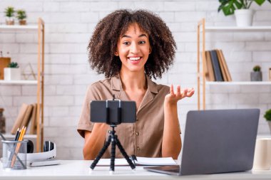 Modern hobi ve blog konsepti. Mutlu Afro-Amerikan kadın web kamerasına bakıyor oturma odasının iç tarafında oturuyor.