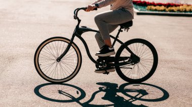 Şehir tarzı, çalışma şekli ve modern şehirde çevre taşımacılığı. Milenyum çalışanı ya da işadamı yaz parkında bisiklet sürüyor, yolda, dışarıda, yan tarafta, boş alanda gölgesi var,