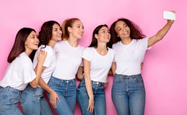 Neşeli Karışık Milenyum Kadınları Cep Telefonu ile Selfie Yapıyor Pembe Stüdyo Arkaplanının Üzerinde Duruyorlar. Bir grup kadın birlikte poz verip kendi resimlerini çekiyorlar. İnsanlar ve Gadget
