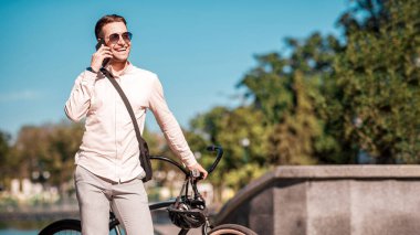 Parktaki yakışıklı hippi. Bisikletli dost canlısı iş adamı telefonda, dışarıda, kopyalama alanında konuşuyor.