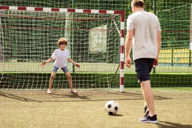 Aktif Boş Zaman. Baba ve çocuğun birlikte futbol oynadığı portre, ayakta duran ve gol kaydeden küçük adam top bekleyen, el sallayan, dışarıda aile maçı yapan yetişkin adam ve çocuk.