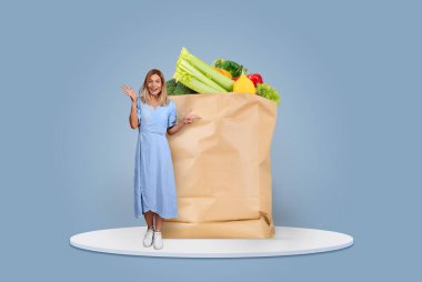 Neşeli bir müşteri, taze meyve ve sebzelerle dolu büyük bir kesekağıdının yanında duruyor. Bu izole zamanlarda yeni normal market alışverişi ve teslimatı somutlaştırıyor..