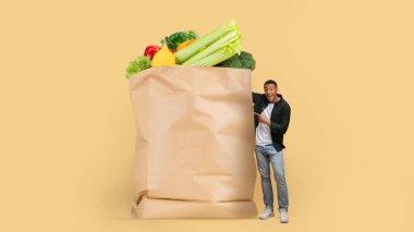 Alışverişçi, çeşitli sebze ve meyvelerle dolu büyük bir kesekağıdının yanında duruyor. Parlak arka plan taze yiyeceklerin canlı renklerini vurguluyor, alışverişin neşesini vurguluyor..