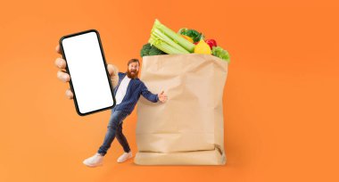Müşteri bir elinde akıllı telefon tutarken içi taze yiyecek dolu büyük bir kese kağıdının yanında duruyor. Bu etkinlik, çevrimiçi market alışverişi ve teslimatının güncel eğilimini vurgular.
