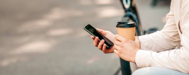 Genç bir adam sıradan bir şekilde kaldırımda oturur, dışarıdan kahve yudumlar. Çevresi canlı bir sokak atmosferiyle çevrili akıllı telefonuna odaklanmış. Tipik bir şehir hayatı, kopyalama alanı.