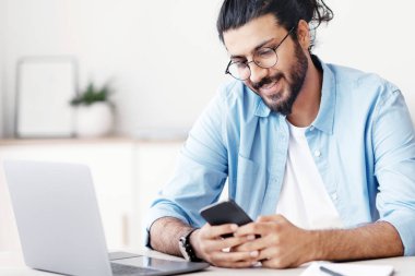 Yakışıklı Doğulu serbest çalışan, ofis masasında oturan ve akıllı telefon kullanan, arkadaşlarıyla mesajlaşan, sosyal medyayı kontrol eden ya da yeni uygulamalara göz atan, mobil iletişimden keyif alan, serbest alan