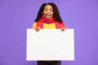 Neşeli Afrikalı Kadın Boş Poster Tutuyor Kış Reklamı Mavi Arkaplanda Duran, Ceket ve Atkı Giyen. Stüdyo Çekimi