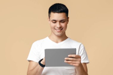 Çalışmak, eğlenmek, dinlenmek ve iletişim kurmak için bir cihaz. Mutlu adam arkadaşlarına yazmak için tablet kullanır, oyun oynar ve bej arka planda izole edilmiş sohbet eder, stüdyo çekimi, boş alan