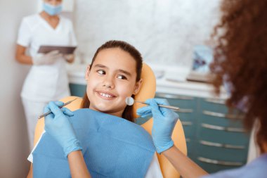 Sağlıklı dişler, stomatoloji ve tıp konsepti. Plastik eldivenli Afrika kökenli Amerikalı dişçi diş kliniğinde gülümseyen İspanyol kız tarafından ağız boşluğu inceleniyor.