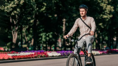 Aydınlık bir günde, genç bir adam renkli çiçeklerle dolu ağaçlarla kaplı bir caddede bisikletini sürüyor. Günlük kıyafetler ve kask takıyor, şehirde aktif bir yaşam tarzını benimsiyor, mekanı kopyalıyor.