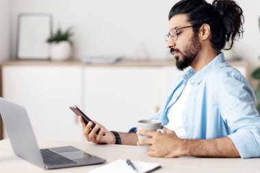 Genç Arap erkek serbest çalışan, akıllı telefon kullanan, kahve içen, İçişleri Bakanlığı 'ndaki işyerinde dinlenen, dizüstü bilgisayar ve not defteriyle masada oturan, projeyi bitirdikten sonra dinlenen,