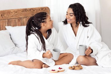 Afro-Amerikan anne ve kızı bornozlu, abur cubur yiyen, kurabiye yiyen, kakao içen, siyah anne ve çocuğu seven, evde birlikte vakit geçiren, boş alan arayan mutlu bir anne ve kız.