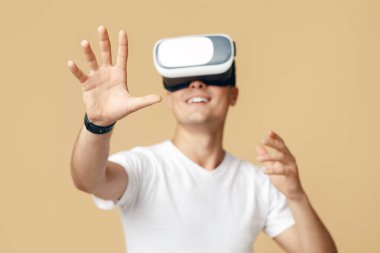 Sanal dünyada iş ve eğlence ve insan duyguları. Modern oyunda oynayan ve elini kaldıran VR gözlüklü heyecanlı adam, bej arka planda izole edilmiş, stüdyo çekimi, boş alan.