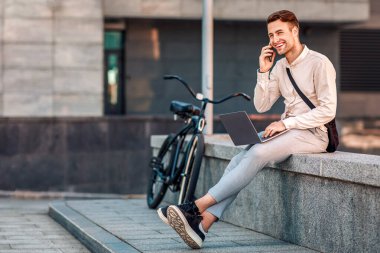 Meşgul adam dışarıda iş sorunlarını çözüyor. Gülümseyen adam akıllı telefonda konuşuyor ve şehirde bilgisayarla çalışıyor.